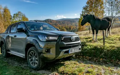 Toyota Hilux GR Sport na tle jesiennych wzgórz, obok stoi koń.
