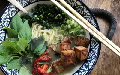 En skål med vegetarisk ramen med nudlar, tofu, grönsaker och basilika.