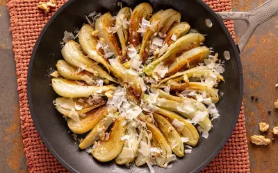 Finocchi in padella dorati e caramellati, guarniti con scaglie di formaggio e noci croccanti. Un piatto semplice e gustoso.