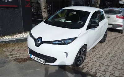 Białe Renault Zoe stoi zaparkowane na chodniku z kostki brukowej.