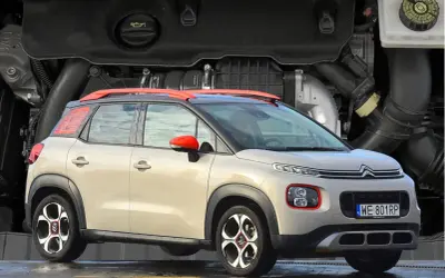 Nowy Citroen C3 2025 w beżowym kolorze z czerwonymi akcentami, prezentowany na tle silnika.