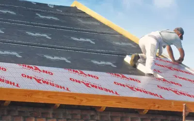 Pracownik montuje izolację nakrokwiową na dachu, układając warstwy materiału termoizolacyjnego.