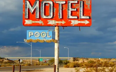Stary, zniszczony neonowy szyld "MOTEL" i "POOL" na tle burzowego nieba. Obok droga i most.