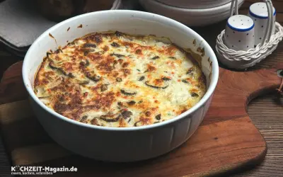 Herzhafter Kohlrabi-Auflauf mit Pilzen und Käse überbacken, serviert in einer weißen Auflaufform auf einem Holzbrett.