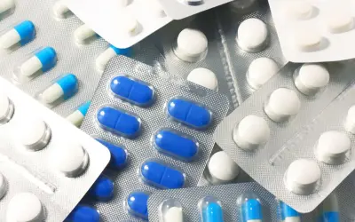 Blistry z białymi i niebiesko-białymi kapsułkami oraz okrągłymi białymi tabletkami, jak polopiryna.