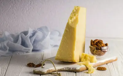 Kawałek sera Grana Padano, czy to parmezan? Obok orzechy pekan i błękitna tkanina.