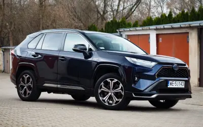Ciemnoniebieski Toyota RAV4 Hybrid zaparkowany przed garażami.