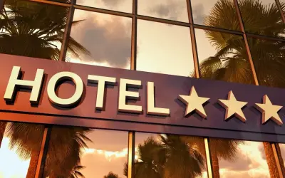 Napis "HOTEL" z trzema gwiazdkami na tle odbijających się palm i nieba.