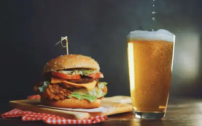 Un succulento hamburger con formaggio fuso e lattuga, accompagnato da una birra bionda spumeggiante.