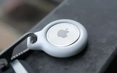 Biały AirTag od Apple, z logo i napisem "Designed by Apple in California". To urządzenie, które pomoże Ci odnaleźć zgubione przedmioty.