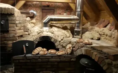 Frisches Brot wird im Pizzaofen gebacken. Mehrere Laibe liegen bereit, einige sind schon im Ofen.