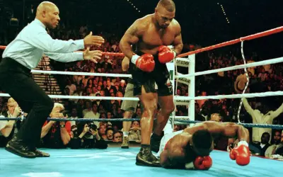 Mike Tyson stands over a fallen opponent, his powerful physique and impressive mike tyson arm length evident. The referee signals the end of the match.