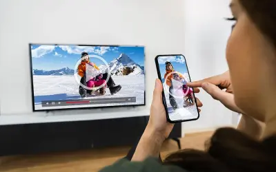 Oglądanie filmu z telefonu na TV przez WiFi. Dzieci zjeżdżają na sankach na ekranie telewizora i smartfona.