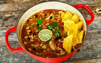 Prawdziwa zupa meksykańska w czerwonym garnku, pełna kurczaka, fasoli, kukurydzy, z limonką i jalapeño. Chrupiące nachos na wierzchu.