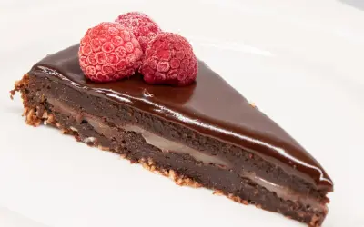 En bit kladdkaka med After Eight-smak, toppad med tre hallon på en vit tallrik.