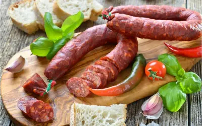 Chorizo co to? Pikantna kiełbasa, chleb, papryczki, pomidor i bazylia na desce.