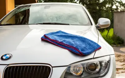 Niebieski ręcznik do osuszania auta leży na masce białego BMW. Idealny do rankingu najlepszych akcesoriów do pielęgnacji samochodu.