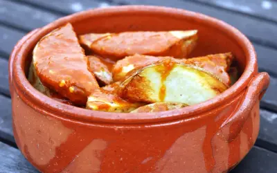 Patatas bravas, pommes de terre croustillantes nappées d'une sauce épicée, servies dans un plat en terre cuite.