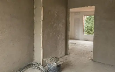 Ściany w trakcie prac wykończeniowych, na których widać świeże tynki cementowo wapienne. W wiadrze przygotowana zaprawa.