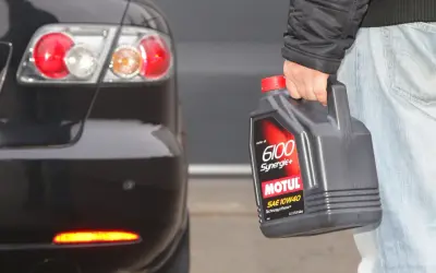 Osoba trzyma olej Motul 6100 Synergie+ SAE 10W40 obok tylnej części czarnego samochodu. Idealny wybór, by dobrze dobrać olej.