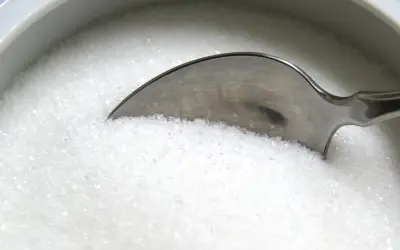 Une cuillère dans un bol de sucre blanc, rappelant les dangers du cholestérol, du sucre ou du sel pour la santé.