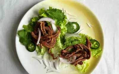 Crujiente oreja de cerdo frita servida sobre lechuga con cebolla morada, cilantro y jalapeño.
