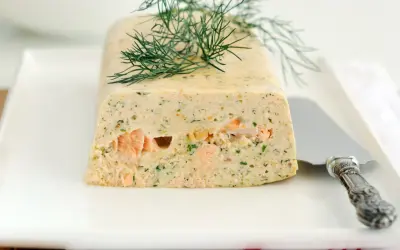 Elegancka terrina z łososia, ozdobiona gałązką koperku, prezentuje się apetycznie na białym talerzu.
