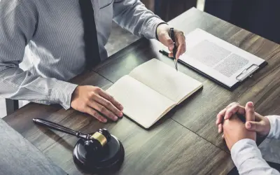 Avvocato e cliente discutono, con un martelletto da giudice e un quaderno aperto. Il ctu significato è fondamentale per la giustizia.