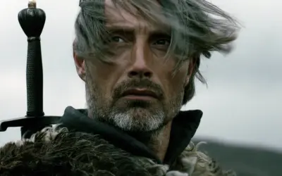 Mads Mikkelsen mit Schwert und Pelzmantel, ein Bild, das an seine Rollen in Filmen und Serien erinnert.