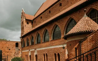 Zamek kapituły warmińskiej w Fromborku, z ceglanymi murami, arkadowymi oknami i charakterystycznym dachem.