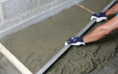 Ręce w rękawiczkach wyrównują świeży styrobeton za pomocą łaty.