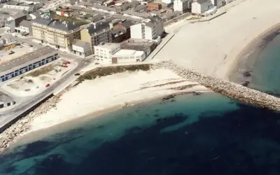 Vista aérea de la playa Penoural en Burela, con edificios urbanos y el mar azul turquesa.