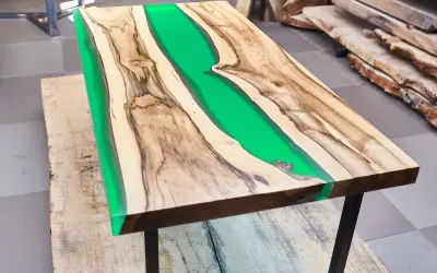 Tavolo con resina verde brillante tra venature di legno. La differenza tra levigatura e lucidatura è evidente nella finitura liscia e riflettente.