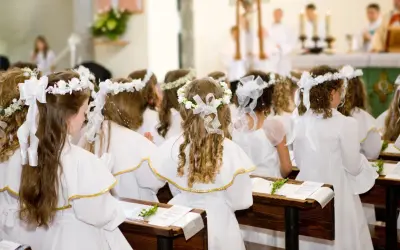 Dziewczynki w bieli, z wiankami na głowach, czekają na uroczystość. Krótkie życzenia na komunię dla nich.