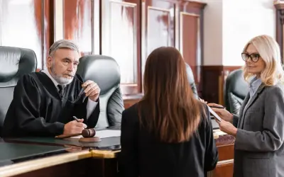Sędzia w todze słucha zeznań, gdy prawniczka notuje. Rozprawa sądowa w toku.