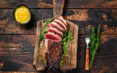 Perfekt gegarte Entenbrust mit rosa Kern, auf einem Holzbrett mit Rucola, dazu eine Schale mit Sauce und ein Gabel. Die Kerntemperatur der Entenbrust ist ideal.