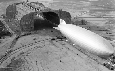 Ogromny hangar lotniczy i sterowiec Hindenburg na płycie lotniska.