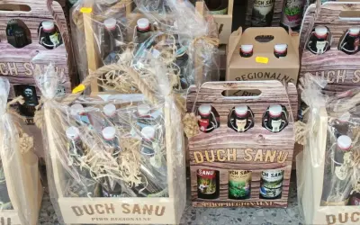 Drewniane skrzynki i opakowania z butelkami regionalnego piwa "Duch Sanu", ozdobione sznurkiem i folią.