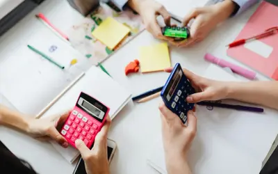 Dłonie trzymające kalkulatory i materiały do nauki matematyki.