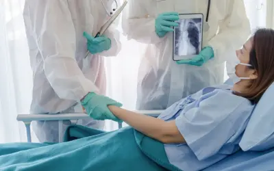 Lekarze w kombinezonach ochronnych wspierają pacjentkę w szpitalu, pokazując jej zdjęcie płuc na tablecie. Nadzieja na powrót do zdrowia dzięki leczeniu, być może z użyciem remdesivir.