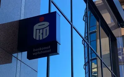 Niebieski szyld PKO BP z napisem "bankomat wpłatomat" na tle szarej ściany i błękitnego nieba. To jak eliksir dla Twoich finansów.