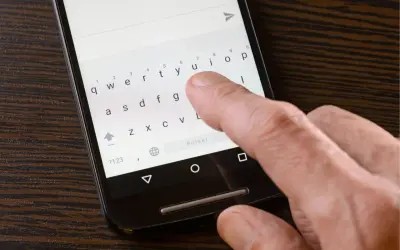 Dłoń pisze na smartfonie, klawiatura pokazuje brak polskich znaków w sms.