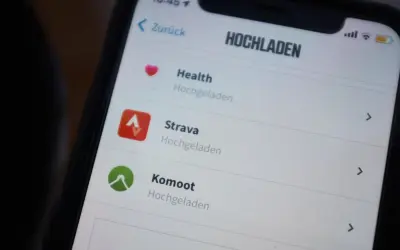 Na ekranie telefonu widać aplikację Strava, obok niej ikonę "Hochgeladen".