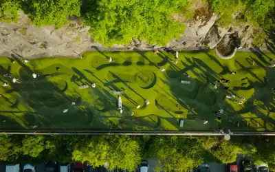 Folk spelar minigolf i Nacka Strand. En grön bana med hinder och skuggor från träden.
