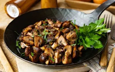 Gebratene Champignons in einer Pfanne, garniert mit frischer Petersilie. Ein köstliches Gericht, das zum Genießen einlädt.