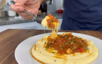 Un tenedor levanta una porción de polenta con tuco, mostrando su textura cremosa y la rica salsa de carne y tomate.