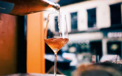 En flaska häller upp ett bubbligt, roséfärgat pet nat i ett elegant glas. En härlig kväll väntar.