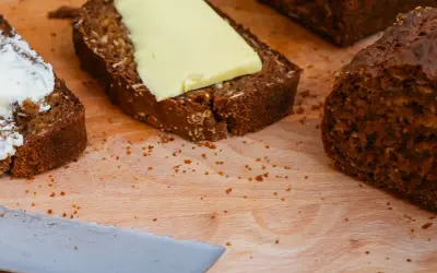 Mörkt bröd med smör och en skiva med yoghurt på en skärbräda.