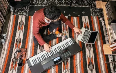 Mężczyzna gra na keyboardzie Casio, obok laptop i słuchawki.