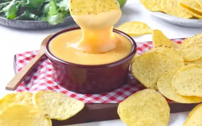 Un totopo se sumerge en un cuenco de crema de queso fundido, rodeado de más totopos.